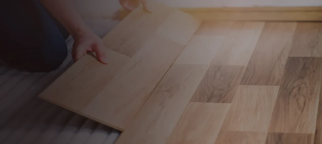 A person installing State Floors wooden laminate flooring, carefully aligning planks on top of underlayment near a wall in Rhode Island.