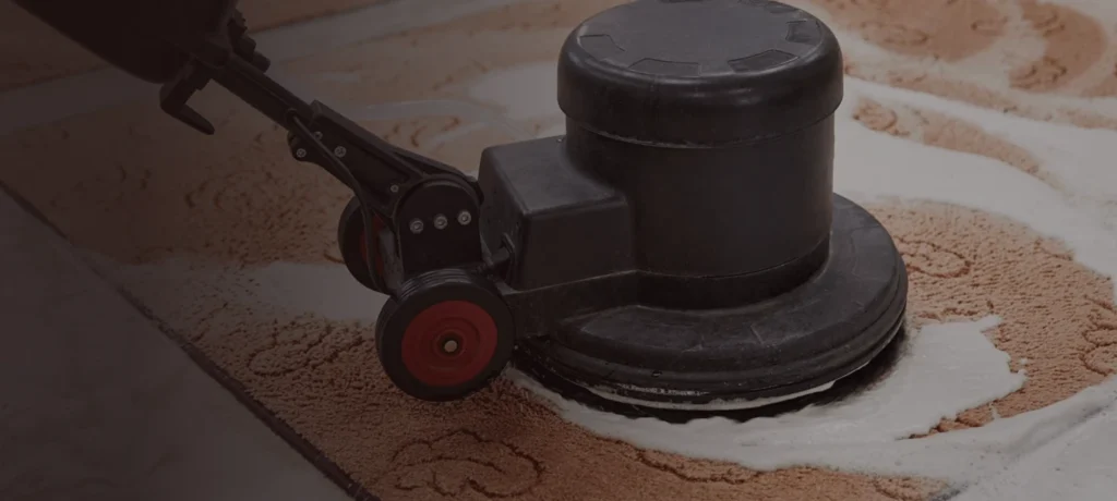 A close-up of a carpet cleaning machine scrubbing a patterned carpet at State Floors in Rhode Island, producing white foam as it cleans the flooring.