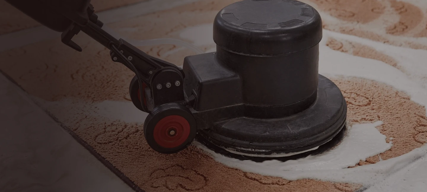 A close-up of a carpet cleaning machine scrubbing a patterned carpet at State Floors in Rhode Island, producing white foam as it cleans the flooring.